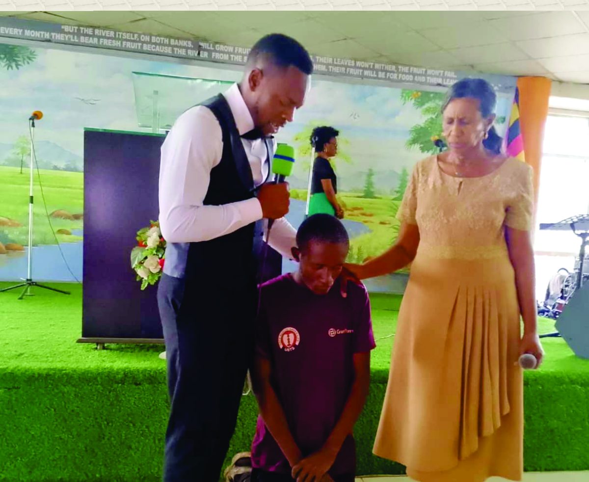Ministers laying hands in prayer on a kneeling youth during an anniversary thanksgiving service