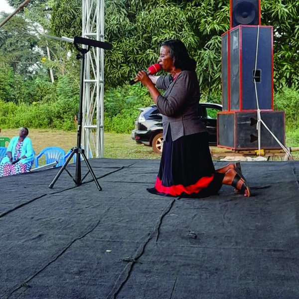 Pastor Agatha ministering on her knees at an outdoor meeting